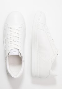 Zapatillas de cuero blanco que presentan un upper texturizado, cordones planos, una suela acolchada y un diseño minimalista en la lengüeta y el lateral.