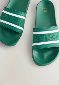 Grüne Rutschsandalen mit strukturierten, gemusterten Riemen, die weiße Akzentstreifen aufweisen. Hergestellt aus glattem, synthetischem Material, im flachen Sohlen-Design.
