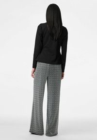 Melns garām piedurknēm top ar pepluma detaļu, kombinēts ar plašām, pelēkās un baltās krāsās rakstainām platām biksēm, kas izgatavotas no mīksta, teksturēta auduma.