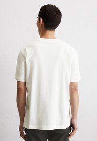 Weißes Baumwoll-T-Shirt mit kurzen Ärmeln, rundem Halsausschnitt und geradem Saum. Der Stoff wirkt glatt mit einer subtilen Textur.