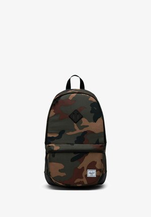 Sac à dos avec motif camouflage vert, marron et noir, poche avant zippée, boucle de poignée noire et écusson logo carré blanc en bas.