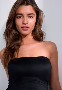 Sort stropløs top lavet af glat stof, med en tætsiddende pasform og en enkel, ren halsudskæring. Naturligt lys fremhæver teksturen.