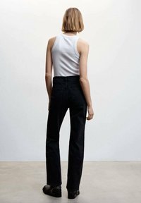 Jean noir taille haute avec une jambe droite, en denim. Associé à un haut sans manches blanc, vu de dos, sur un fond neutre.