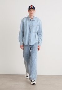 Cămașă din denim de un albastru deschis și blugi asortați, croială supradimensionată, completată cu adidași negri, albi și bleumarin. Căciulă solidă bleumarin cu detalii logo.