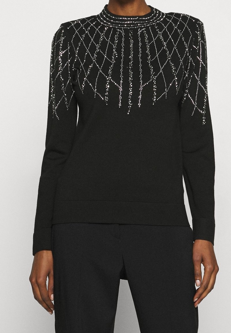 Pull noir à manches longues avec un col rond, orné de perles argentées formant un motif géométrique sur le buste et les épaules.