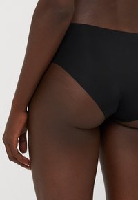 Magas derekú fekete bikini alsó sima textúrával és letisztult vonalakkal, amelyen nincsenek látható fémrészek vagy minták, hátulról bemutatva.