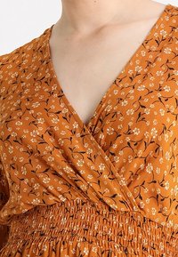 Rustonväriinen mekko, jossa on kukkakuvio, vyötärön kietova malli, V-pääntie ja rypytetty vyötärö. Kevyt kangas, lyhyet hihat.