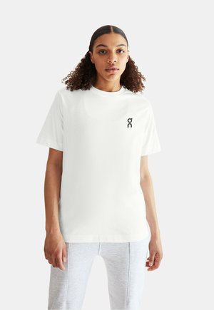 Vit t-shirt med rund hals och korta ärmar, med en svart logotyp på vänster bröst. Mjuk tyg med en avslappnad passform.