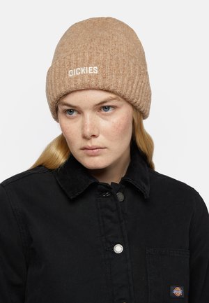 Brun ribbet strikket hue med broderet "DICKIES" logo; båret med en sort kordfløjl jakke med trykknapper og en lomme med patch.