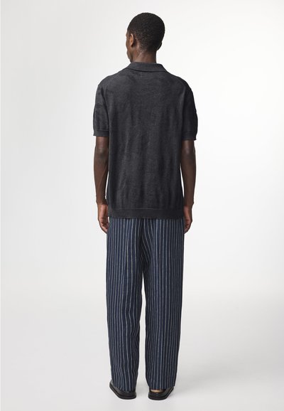 Zwarte korte mouwen polo met een textuurpatroon, gecombineerd met marineblauwe gestreepte wijde broek en zwarte schoenen. Eenvoudig, casual design.