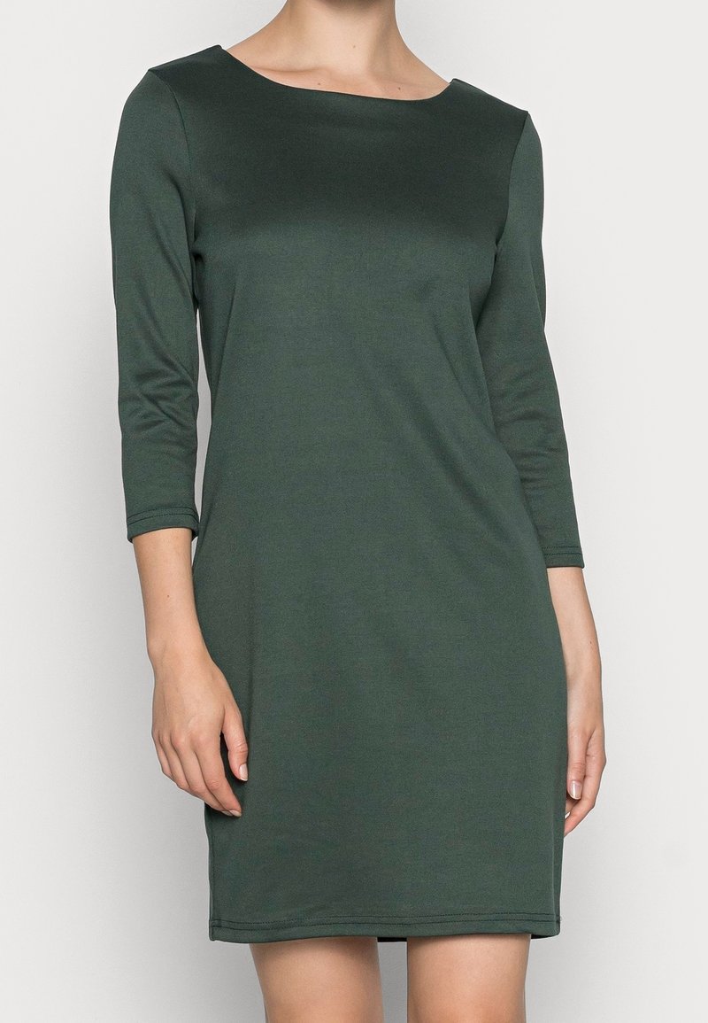 Tumma vihreä, polvimittainen mekko, jossa on kolme neljänneksen hihatableja, valmistettu sileästä ja joustavasta kankaasta. Mekossa on pyöreä pääntie ja yksinkertainen muotoilu.