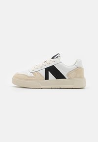 Sneaker bianco con accenti in suede beige, logo nero e suola in gomma texturizzata. Presenta lacci rotondi e colletto imbottito per il comfort.