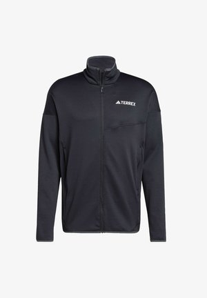 Veste zippée noire en tissu doux, dotée d'un col montant, d'une fermeture éclair sur toute la longueur et d'une petite poche sur la poitrine. Logo imprimé sur le côté gauche.