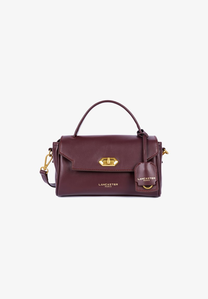Sac à main en cuir bordeaux avec une poigné supérieure, quincaillerie dorée, fermeture à rabat à l'avant et un détail de tag de bagages. Bandoulière réglable incluse.