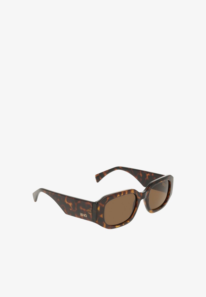 Lunettes de soleil écaille de tortue marron avec des montures légèrement arrondies et des verres marron. Elles présentent des branches épaisses avec un logo subtil.