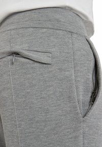 Grijze joggingbroek met een textuurstof, elastische tailleband en een ritssluiting aan de zijkant voor veilige opberging.