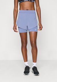 Αθλητικά σορτς σε ανοιχτό μωβ χρώμα με στρωτή σχεδίαση και φαρδύ λογότυπο, με ένα μικρό λευκό λογότυπο της Nike. Φοριούνται με μαύρα αθλητικά παπούτσια.