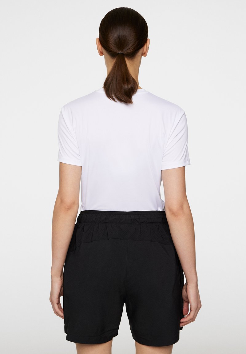 Camicia bianca a maniche corte con scollatura tonda abbinata a pantaloni neri con vita elastica e dettagli arricciati sul retro.