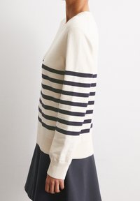Maglione crema con righe orizzontali blu navy, maniche lunghe e orlo a coste. Realizzato in un tessuto morbido, presenta un classico design a girocollo.