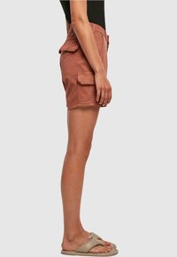Shorts cargo couleur rouille avec poches latérales, fabriqués dans un tissu durable, dotés d'une coupe droite et d'une fermeture éclair à l'avant.