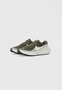 Une paire de chaussures de course Nike vert olive et blanche avec des semelles noires, positionnées côte à côte sur un fond blanc uni.