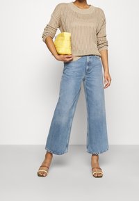 Béžový pletený svetr, světle modré džíny s širokými nohavicemi, žlutá pletená kabelka a sandály s pásky se zlatým akcentem na horním pásku.