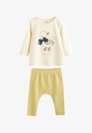 Grietos ilgomis rankovėmis marškiniai su antis atspaudu ir tamsiai mėlyna kaspinu, derinami su geltonomis raukinėmis legginėmis. Minkšta medvilninė medžiaga, laisvas siluetas.