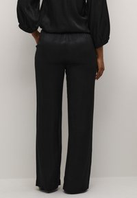 Pantalons noirs à jambes larges en tissu lisse avec une subtile texture en imprimé serpent. Disposent d'une taille élastique pour le confort et une facilité d'enfilage.