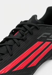 Μαύρο αθλητικό παπούτσι με υφασμένο επάνω μέρος, έντονες κόκκινες ρίγες και μαύρα κορδόνια, με χαμηλή κοπή και μαλακό περίβλημα στον αστράγαλο.