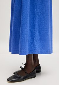 Blaue, strukturierte, knielange Rock mit geradem Schnitt. Kombiniert mit schwarzen, flachen Schuhen mit abgerundeter Spitze und Knöchelbindungen.