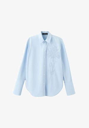 Camicia azzurra chiaro con bottoni, maniche lunghe, ricamo floreale sul lato sinistro, tessuto liscio e orlo arrotondato.