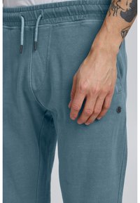 Lyseblå sweatpants lavet af blødt stof med elastisk talje, snoretræk, sidelomme og et lille mærke på låret.