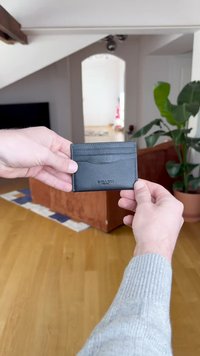 Czarny skórzany etui na karty z wieloma przegródkami i gładką fakturą, ozdobione subtelnym przeszyciem i logo wytłoczonym z przodu.