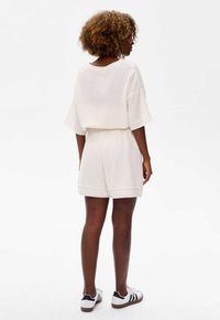 Crème korte mouwen, gebreid topje gecombineerd met bijpassende shorts, met een ontspannen pasvorm en een elastische tailleband. Gedragen met zwartgestreepte witte sneakers.