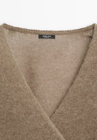 Beige gestrickter Pullover mit V-Ausschnitt, aus weichem, strukturiertem Stoff und mit einem zarten Finish; enthält ein schwarzes Markenlabel am Ausschnitt.