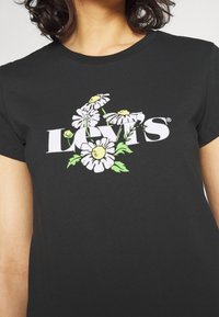 Czarny t-shirt z białym logo "Levi's" otoczonym białymi stokrotkami i zielonymi akcentami. Krótkie rękawy i okrągły dekolt.