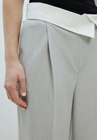 Hellgraue, plissierte Hose mit einem breiten weißen Bund. Glatte Textur mit subtilen vertikalen Streifen, die maßgeschneiderte Designdetails präsentieren.