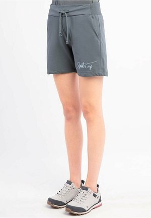 Person trägt dunkelgraue Shorts mit Kordelzug und dem Text "Sport Camp" sowie hellgraue Sportschuhe mit schwarzen und pinken Akzenten.