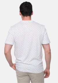 Kortærmet hvid skjorte med et flerfarvet geometrisk mønster. Har en rund halsudskæring og en afslappet pasform. Glat tekstur.