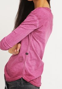 Pitkähihainen paita liukuvärjätyssä purppuran sävyssä, pyöreällä helmalla, sivusaumalla ja logolla alareunan vasemmassa reunassa. Pehmeä pinta.