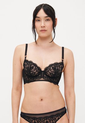 Svart blonde bralette med blomster mønster, gjennomsiktige kopper og dekorativ søm langs kantene. Justerbare stropper og tettsittende underband.