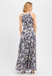 Maxikjole i marineblåt stof med et blomsterprint i creme. Har en halterneck og en let, flydende silhuet. Bagpå er der en detalje med en nøglehul.