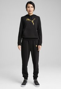 Black hoodie and pants set made of soft fabric, featuring a gold Puma logo on the front. The pants have elastic cuffs and pockets.