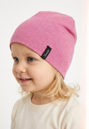 Young child with blonde hair wearing a pink beanie and cream-colored shirt, facing left and smiling slightly.