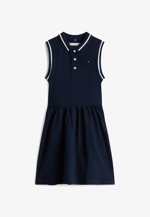 Marineblauwe mouwloze jurk met kraag, een knoopsluiting met drie knopen en contrasterende witte biezen op de kraag en armsgat; rok met plooien.
