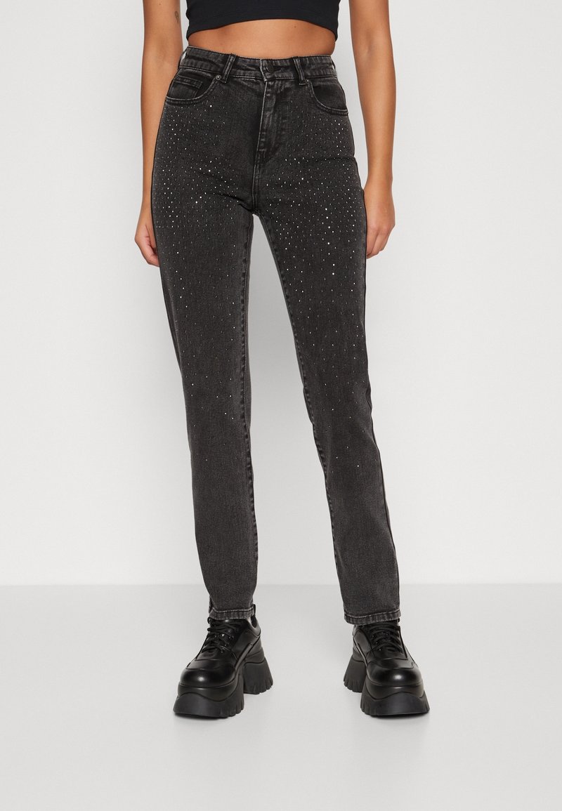 Jean noir taille haute avec de petites décorations en strass, porté avec des chaussures à plateforme noires à lacets et un top court noir.