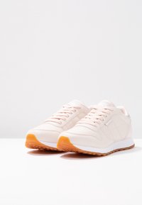 Ljusrosa sportskor med slät syntetisk ovandel, snörning och texturerad sula. Har en kontrasterande orange gummitopp.