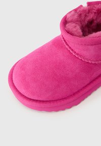 Botín de ante rosa con punta redondeada, forro interior suave y detalles cosidos a lo largo del tobillo. Suela de goma gruesa para mayor tracción.