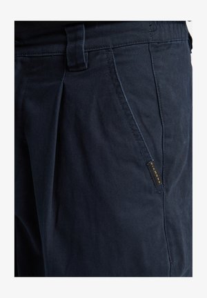 Mörkblå byxor med en slät yta, med rak passform, sidofickor och en guld "Diamond"-etikett på vänster ficka.