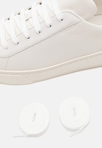 Baskets en cuir blanc avec semelle en caoutchouc texturée et lacets plats blancs. Logo embossé sur le côté. Comprend deux paires de lacets supplémentaires.